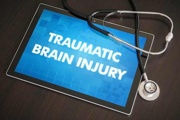 A tablet displaying "TRAUMATIC BRAIN INJURY" on its screen, accompanied by a stethoscope, symbolizing medical attention and diagnosis for brain injury cases.