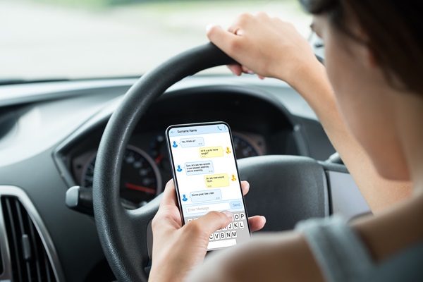 Close-up of young woman sitting inside car, typing a text message on a mobile phone.