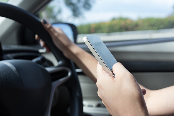 Driver holding a cellphone while steering a vehicle, illustrating distracted driving behavior that increases crash risk and can lead to liability in car accident claims.