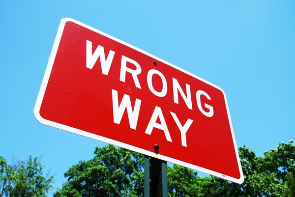 Red “Wrong Way” traffic sign mounted on a post against a clear blue sky, warning drivers of entering a one-way road in the incorrect direction.